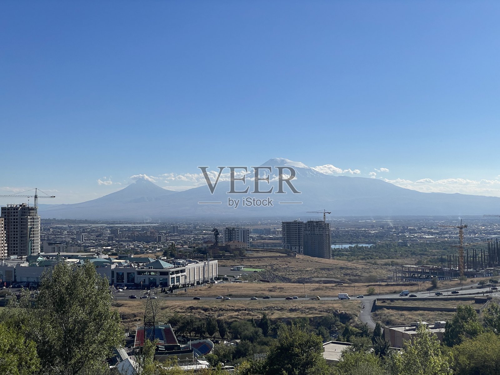 雄伟的阿拉拉特山俯瞰着一座繁华的城市和在晴朗天空下的建筑工地。照片摄影图片