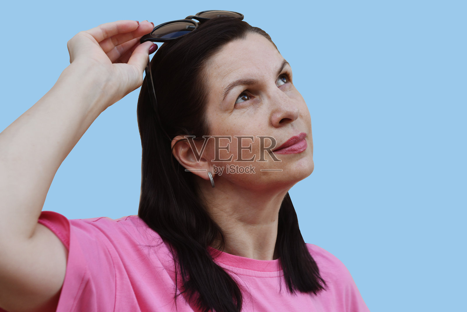 蓝色背景下,戴着太阳镜、穿着粉色T恤的白人棕发女性肖像。照片摄影图片