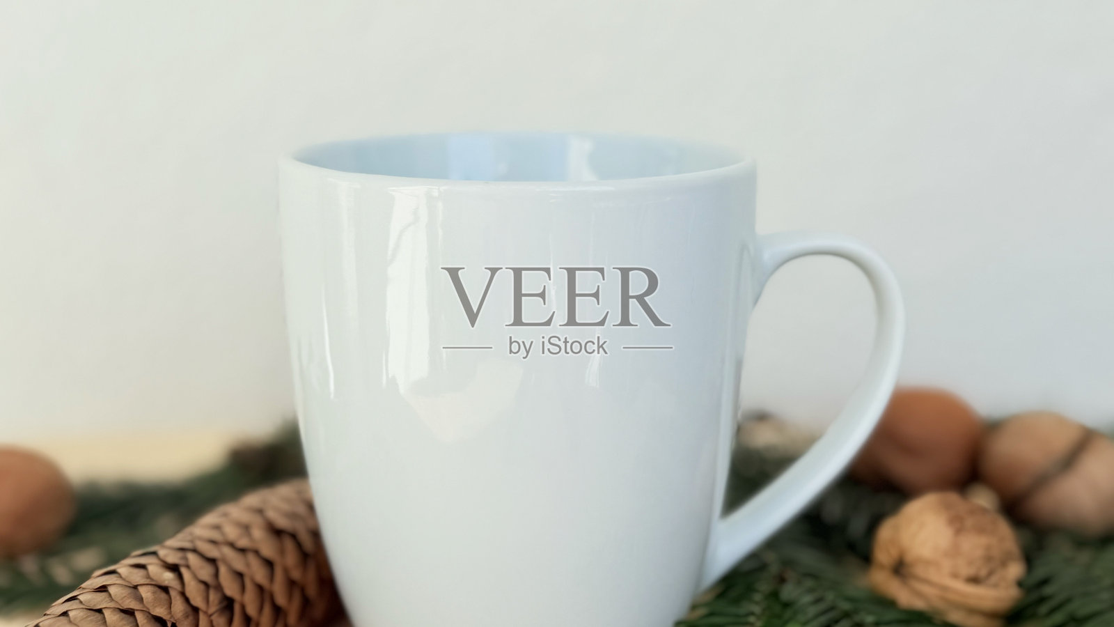 特写白色杯子与松果和胡桃放在常青树枝上 — 温馨的冬季装饰,简约的样板,适合横幅、品牌和模板设计的留白空间照片摄影图片