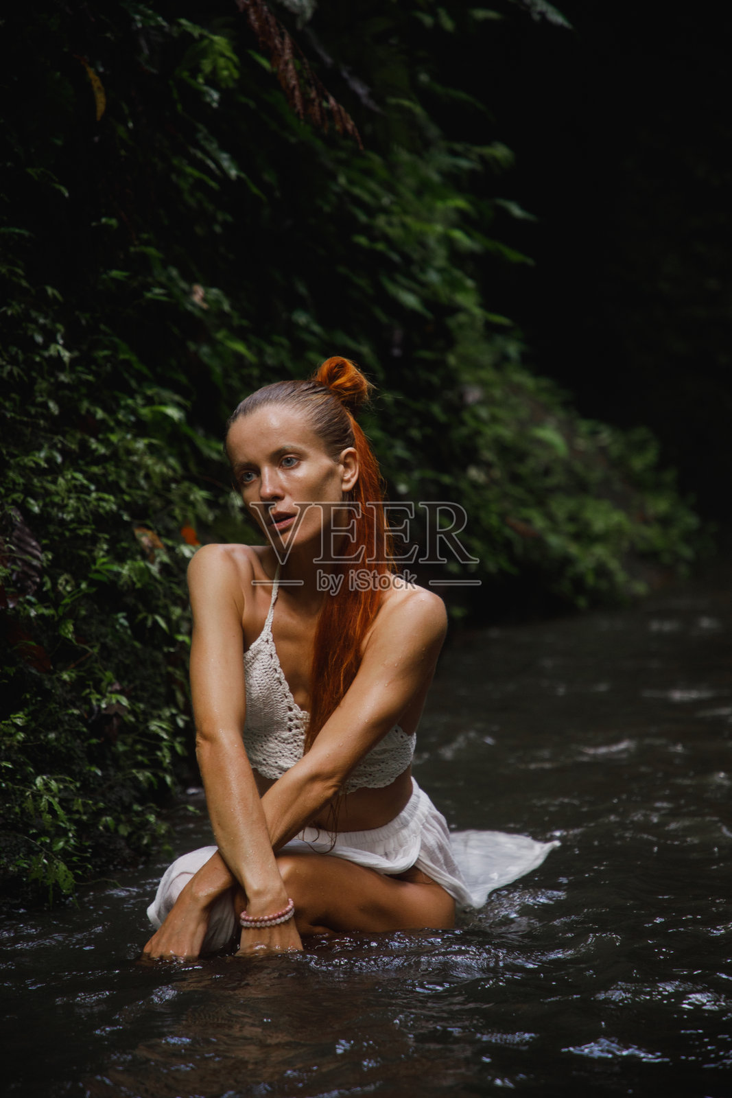 穿着钩针编织上衣的女性坐在浅溪中,置身于大自然中照片摄影图片