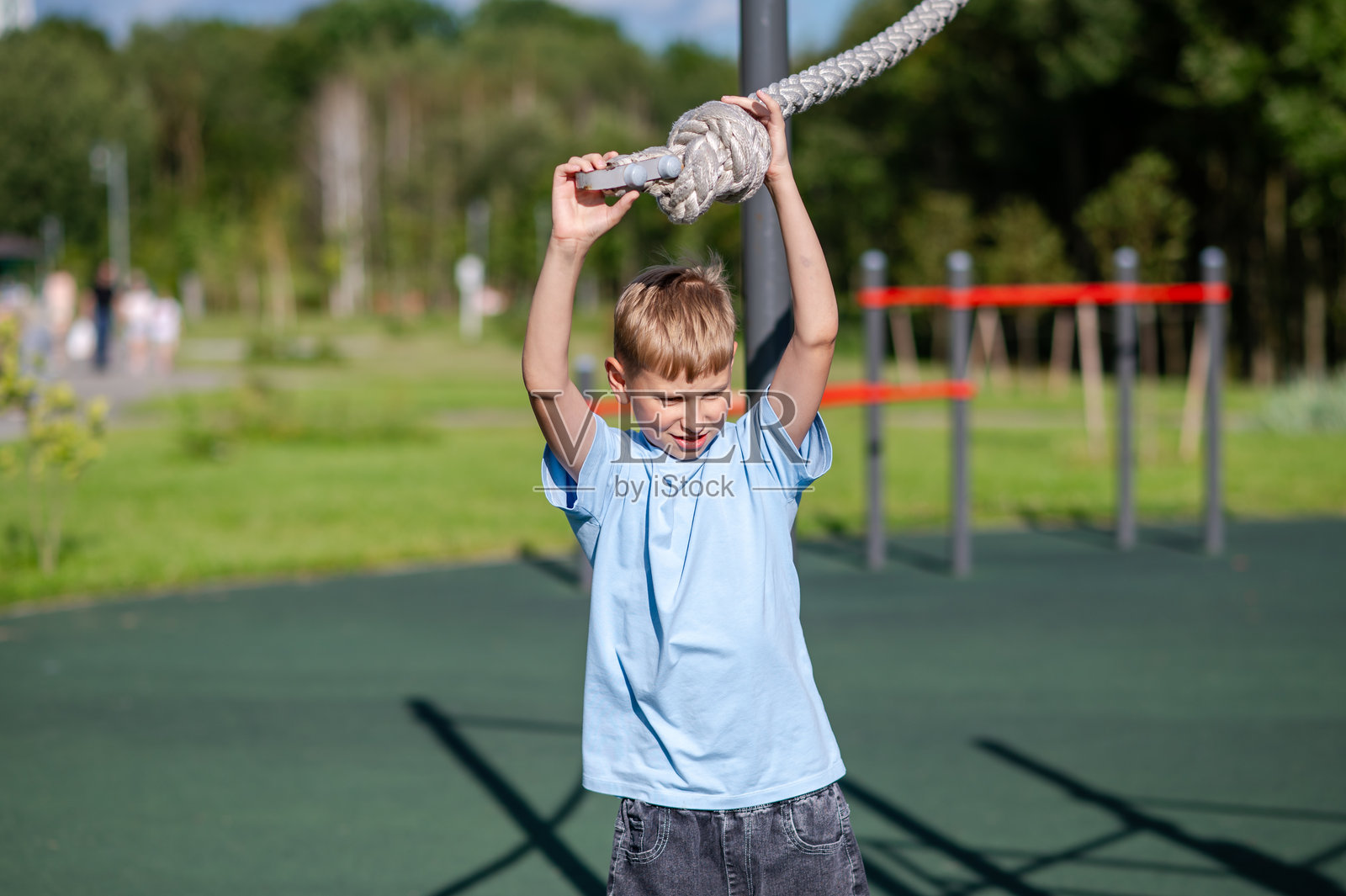 青少年男孩在游乐场上握着绳子,周围有运动器材照片摄影图片