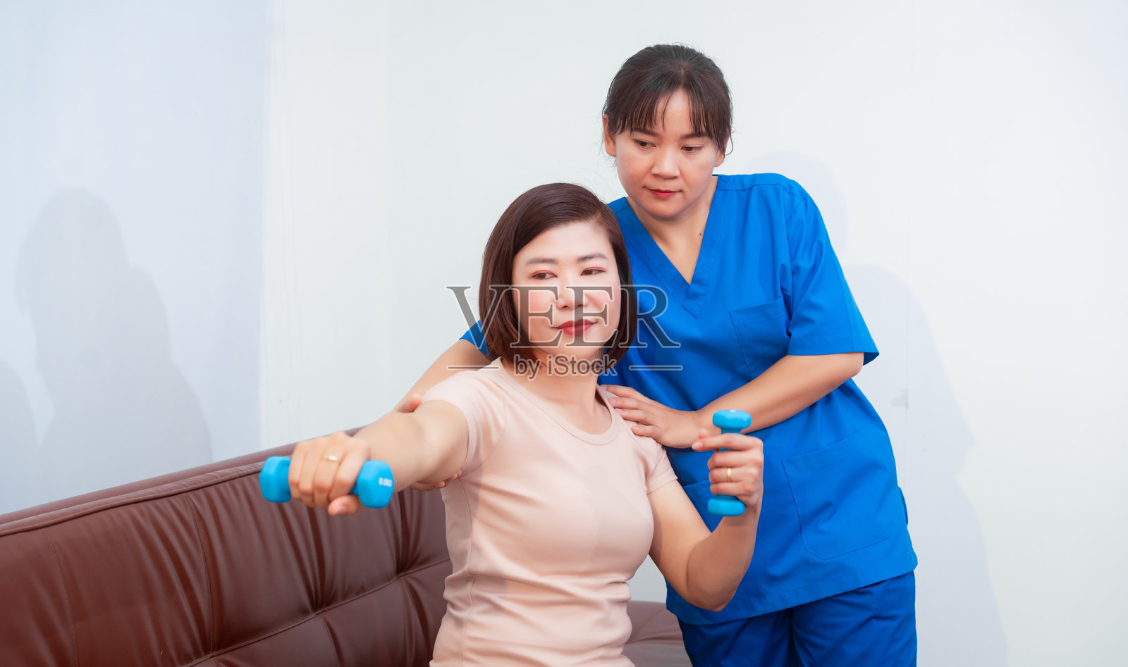 年轻的亚洲护士在医疗机构中协助中年女性患者进行物理治疗,专注于肌肉强化、康复、拉伸和肩部疼痛管理。照片摄影图片