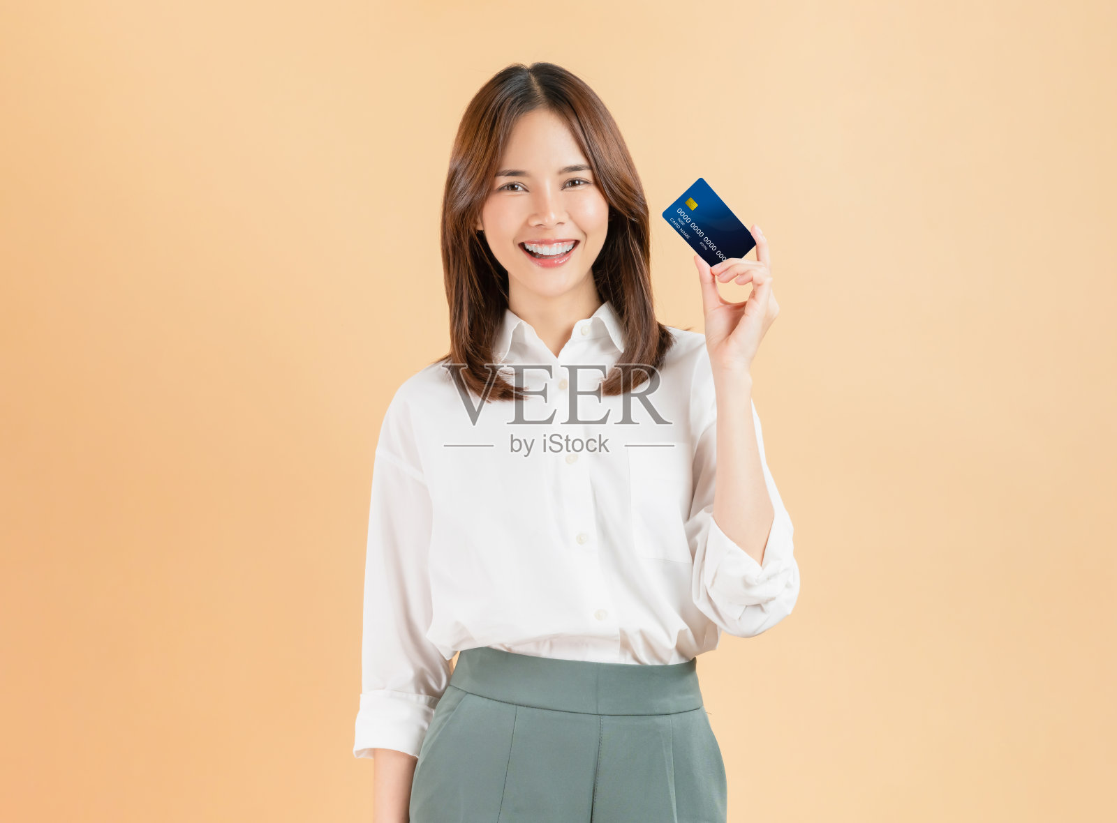 快乐美丽的亚洲女性手持信用卡,背景为米色。照片摄影图片