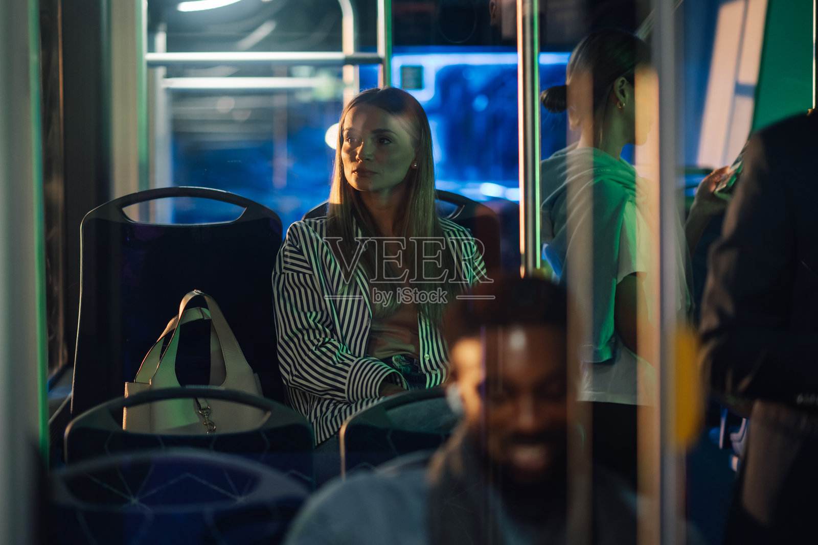年轻女子在夜晚的公交车上坐着,望着窗外。照片摄影图片