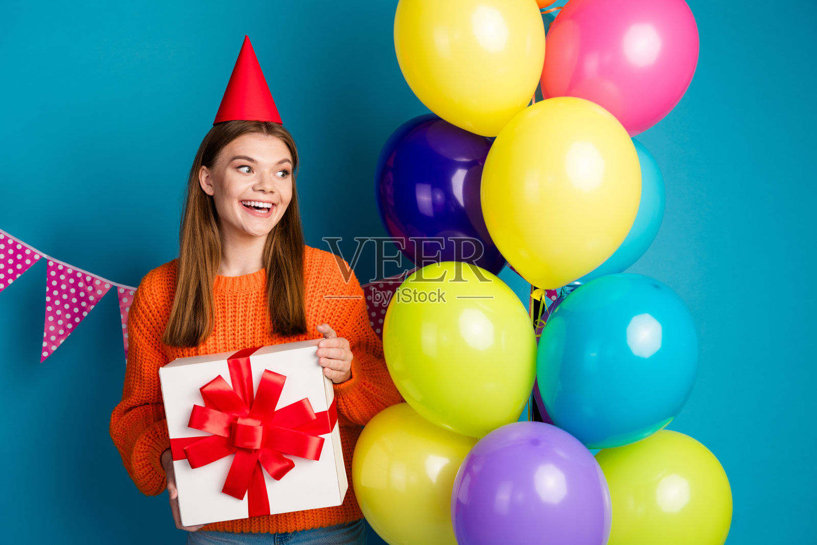 可爱的年轻女性在充满活力的蓝色背景下庆祝生日,周围有五彩缤纷的气球和礼物。照片摄影图片