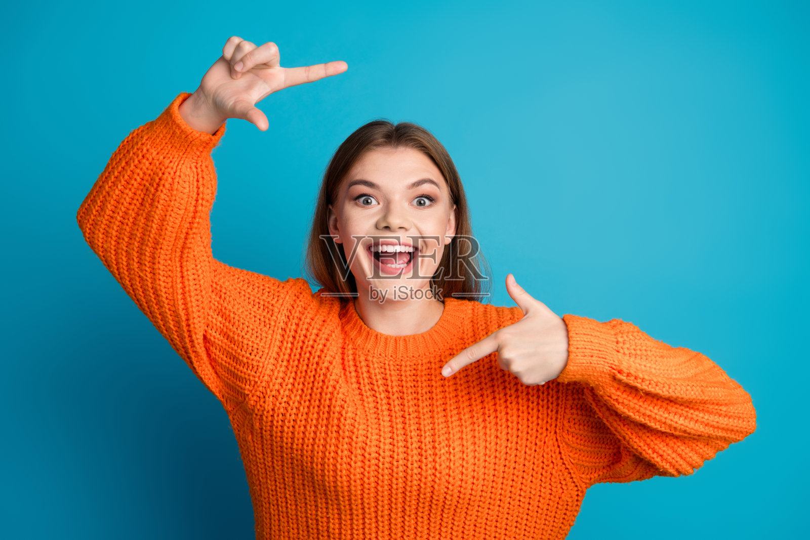 穿着鲜艳橙色毛衣的快乐年轻女性在明亮的蓝色背景前摆姿势,散发着快乐的气息照片摄影图片