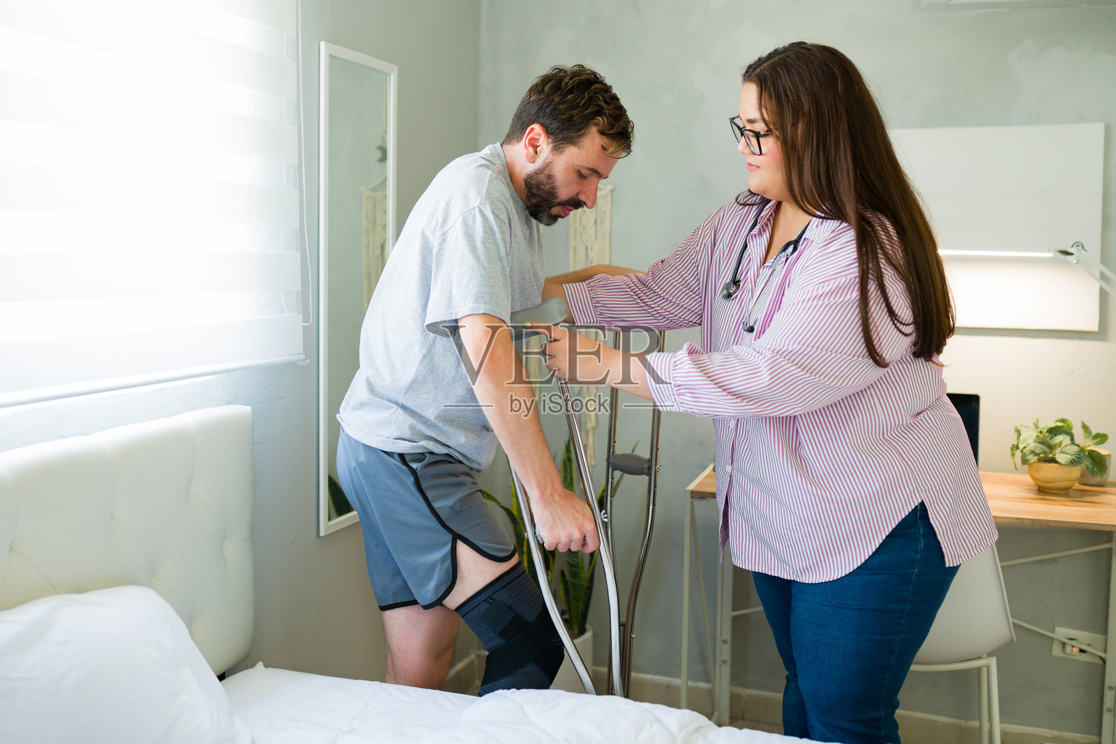 关心的护士在卧室里帮助术后使用拐杖的病人照片摄影图片