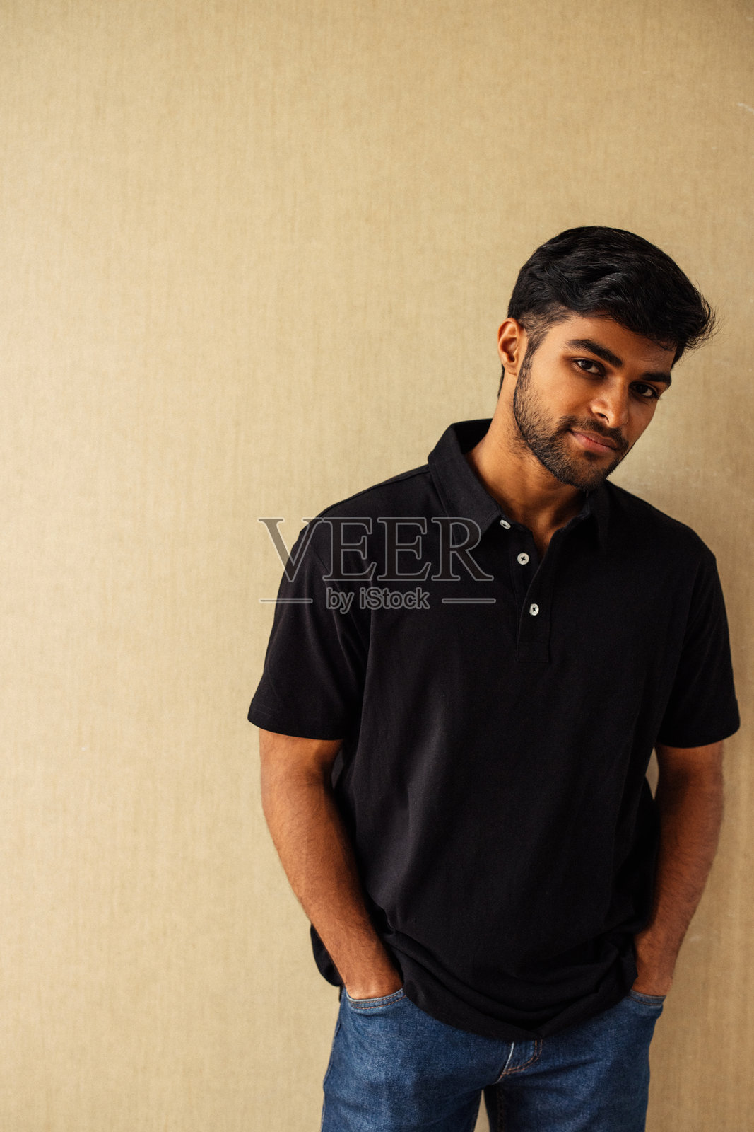 年轻男子穿着黑色衬衫和蓝色牛仔裤,站立姿态随意放松。照片摄影图片