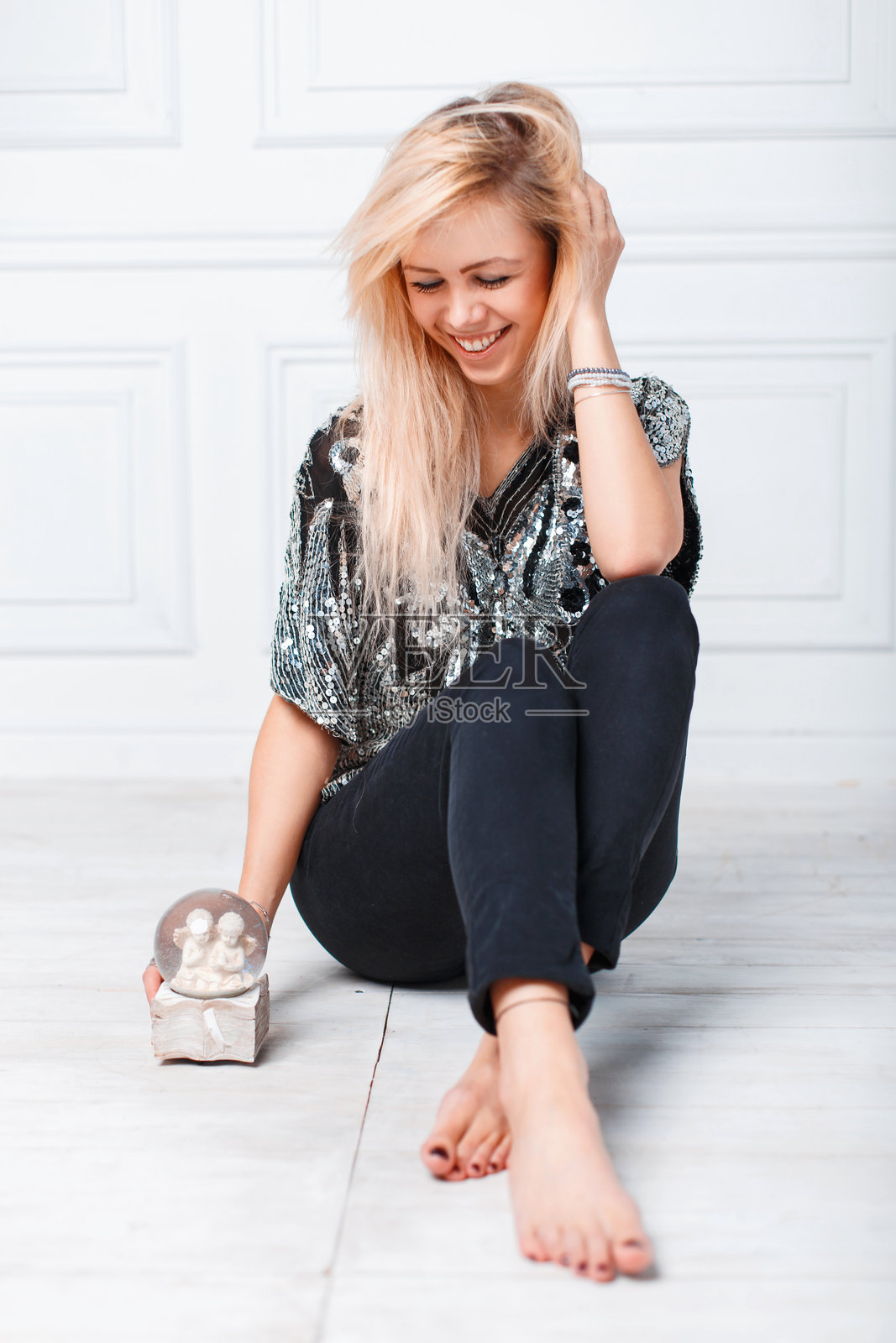 年轻漂亮的金发女孩坐在地板上,手里拿着一个神奇的圣诞球。照片摄影图片