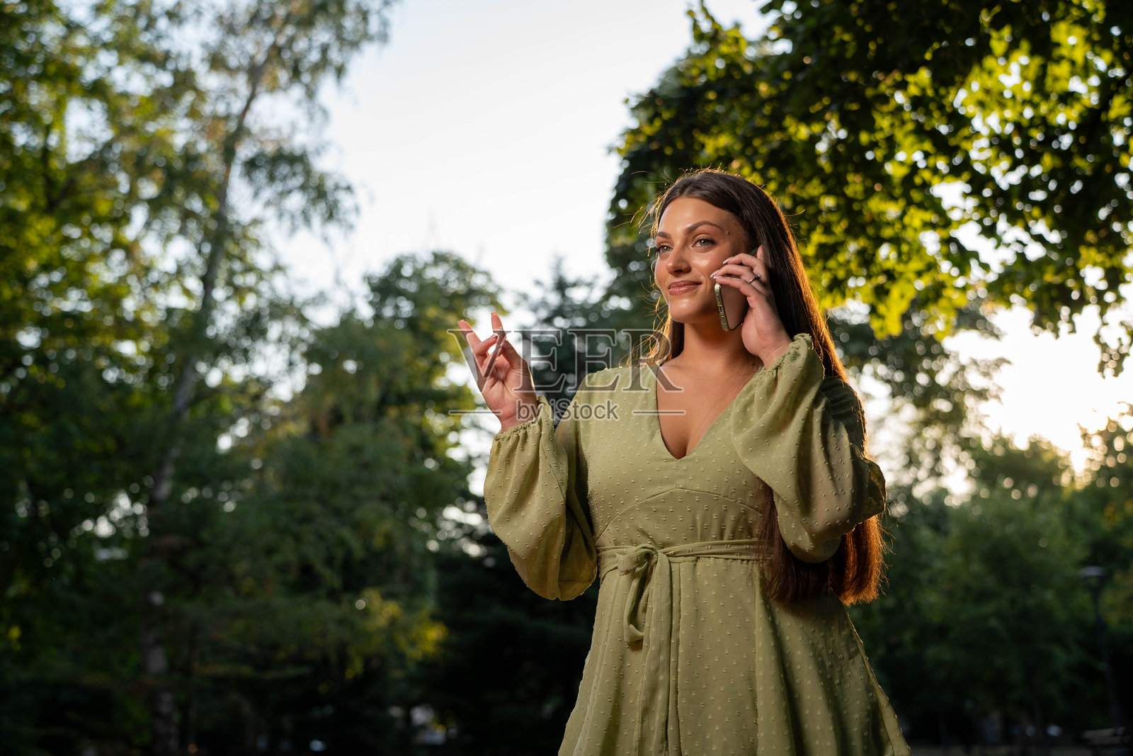 快乐的女人在公园里一边走一边用智能手机通话照片摄影图片