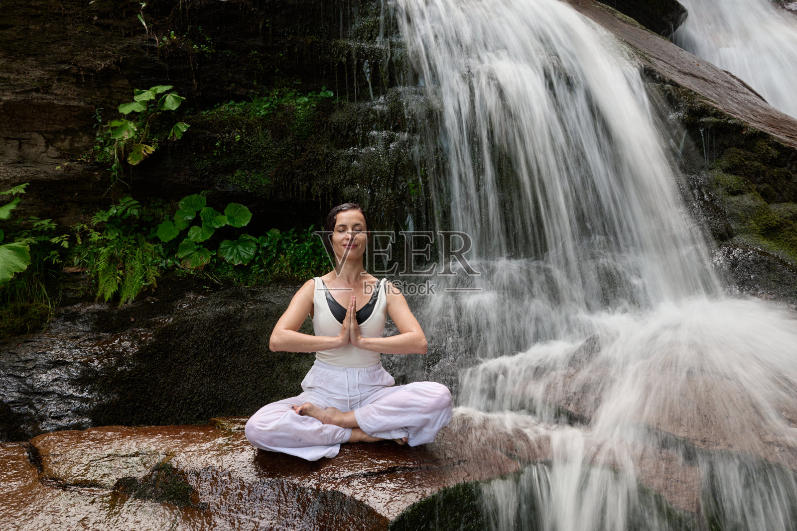 年轻女性坐在热带瀑布下的莲花坐姿中,冥想时展现出平静的力量和正念,完全与自然的能量、宁静和内心的平衡相连接。照片摄影图片