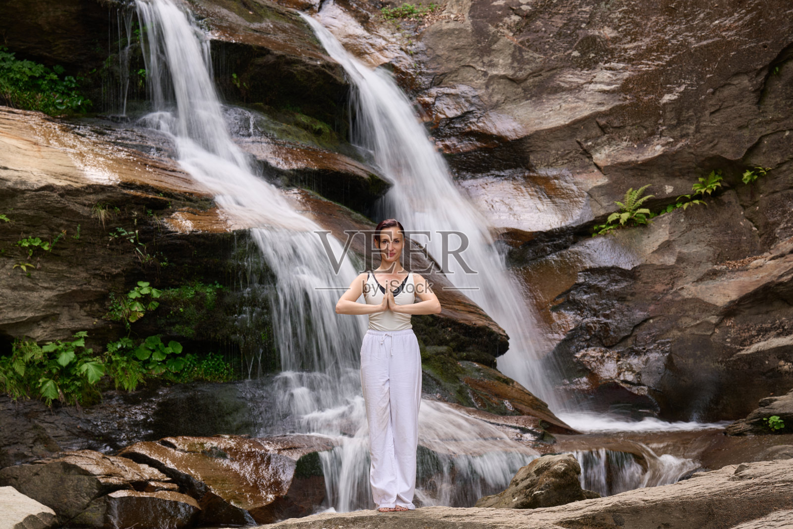 在日落时分,女人在瀑布和河流旁缓慢地练习太极,展现了自然中的和谐、平衡与健身。照片摄影图片