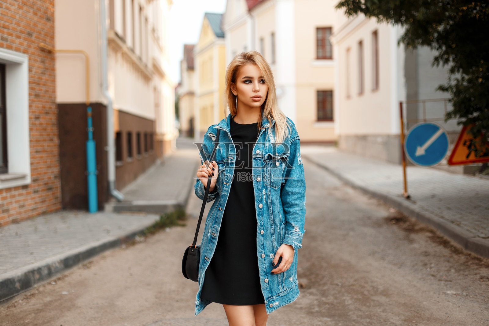 穿着牛仔服的时尚美女手提手袋在街上走。照片摄影图片
