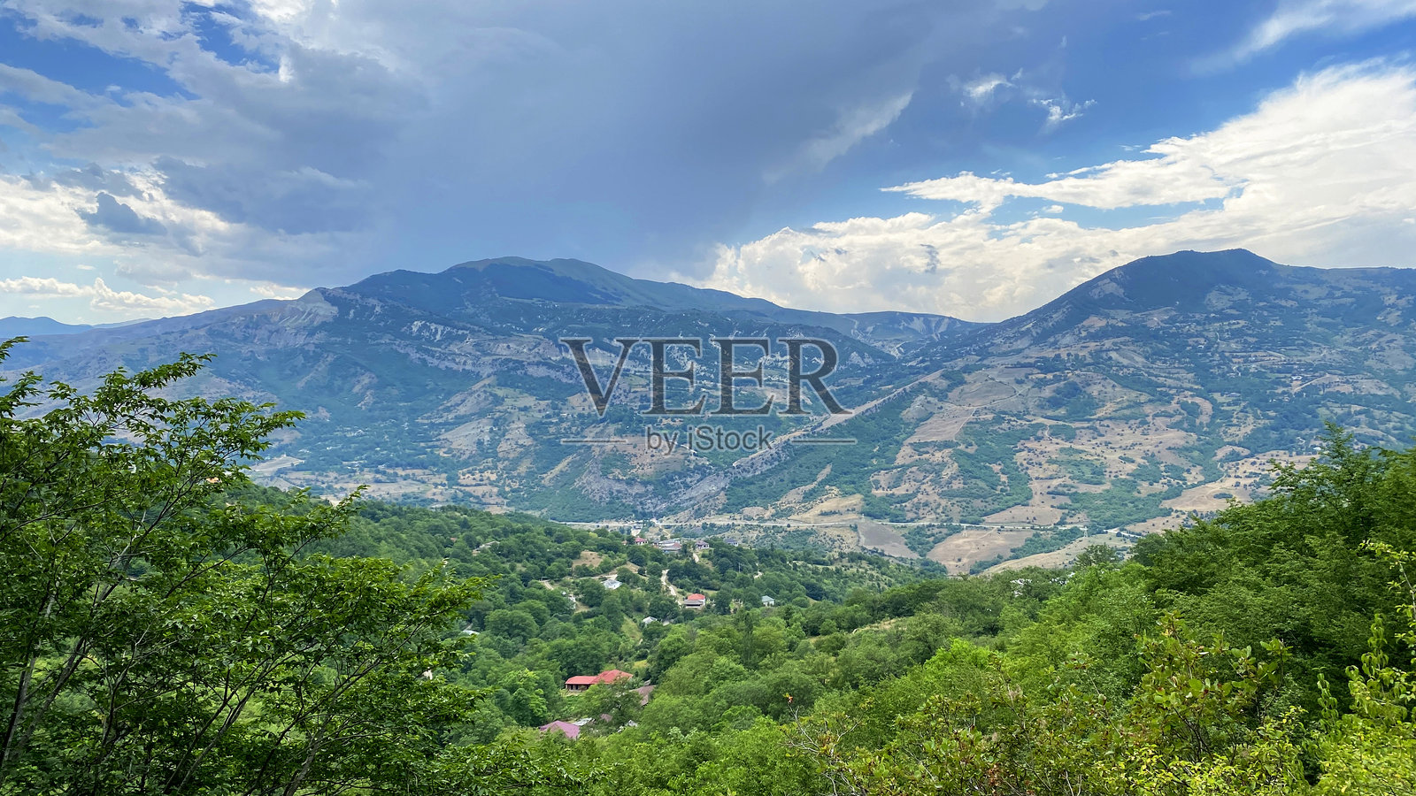 山脉和绿色山谷的鸟瞰图,中间有一个小村庄。这是一次前往阿塞拜疆的旅行。丘陵、斜坡和岩石。照片摄影图片