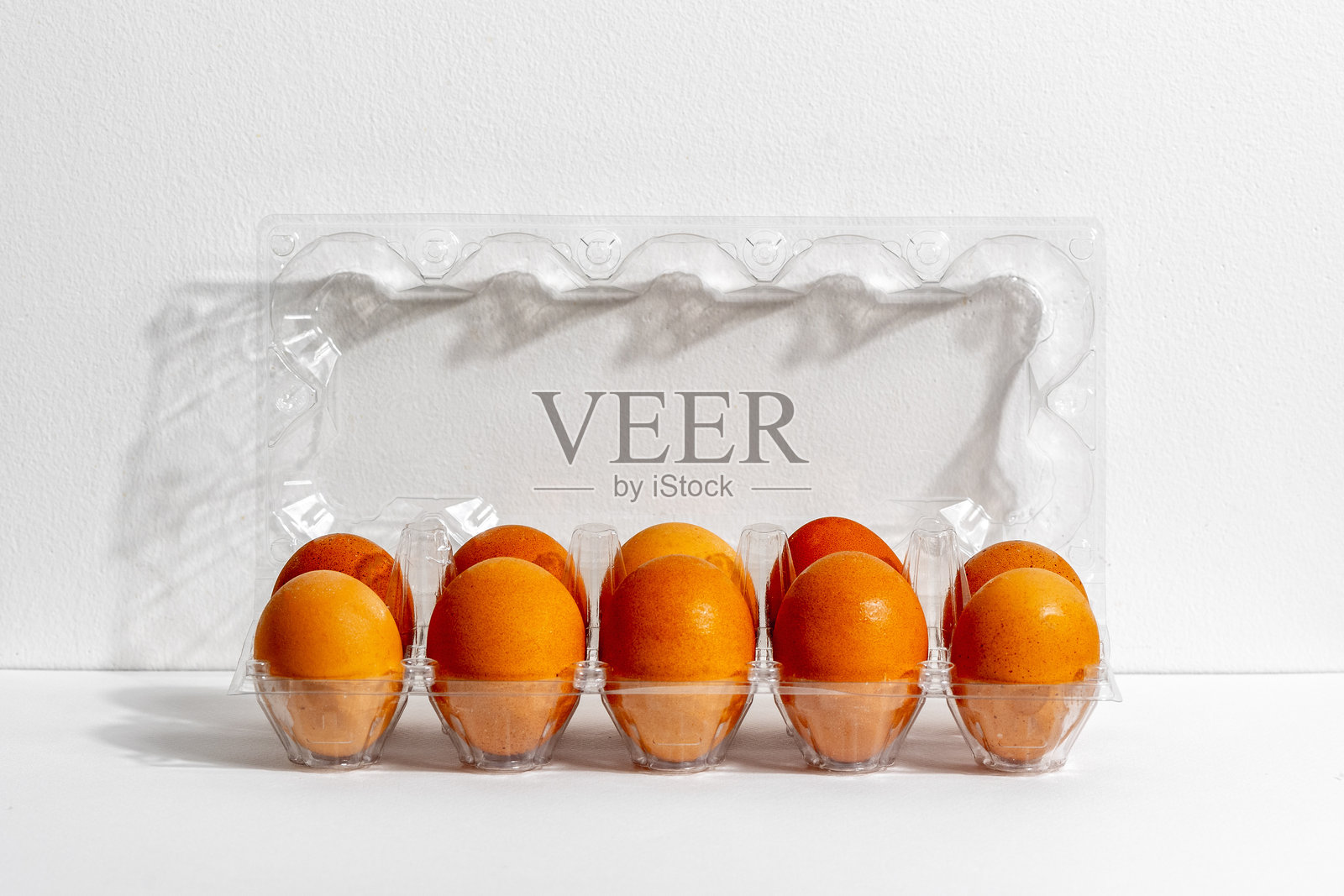 白色背景下透明塑料盒中的橙色鸡蛋照片摄影图片