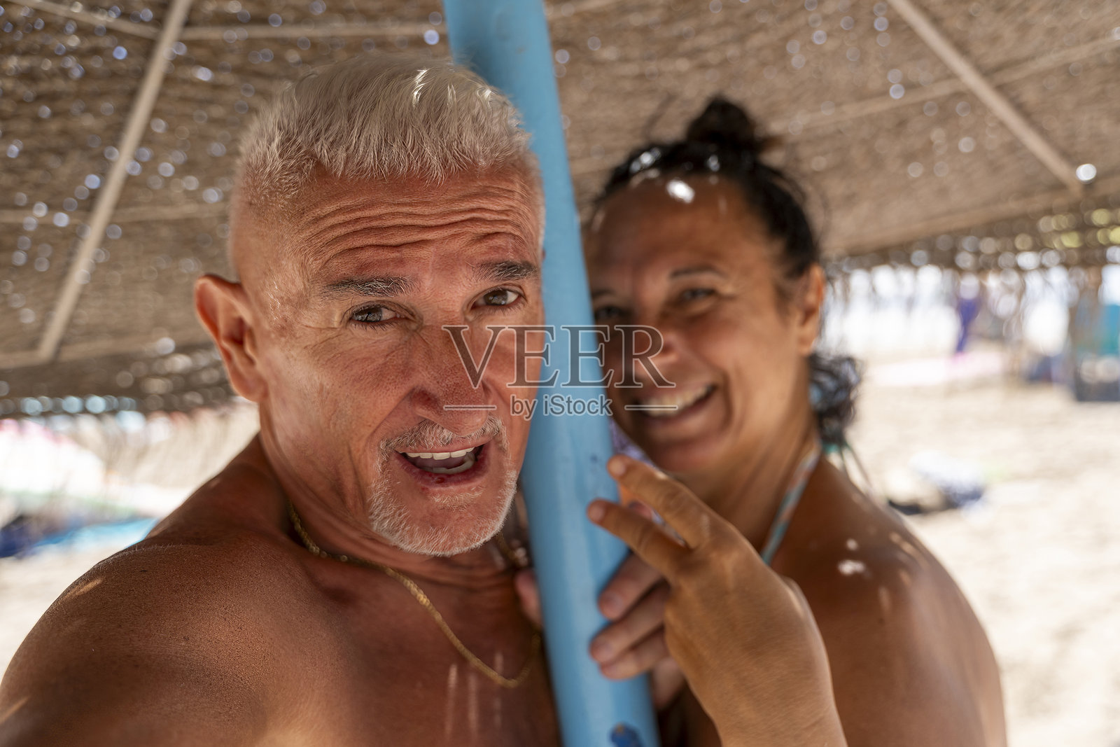 一对快乐美丽的退休夫妇在海滩的草伞下拥抱微笑,拍摄自拍照,享受夏季假期。照片摄影图片