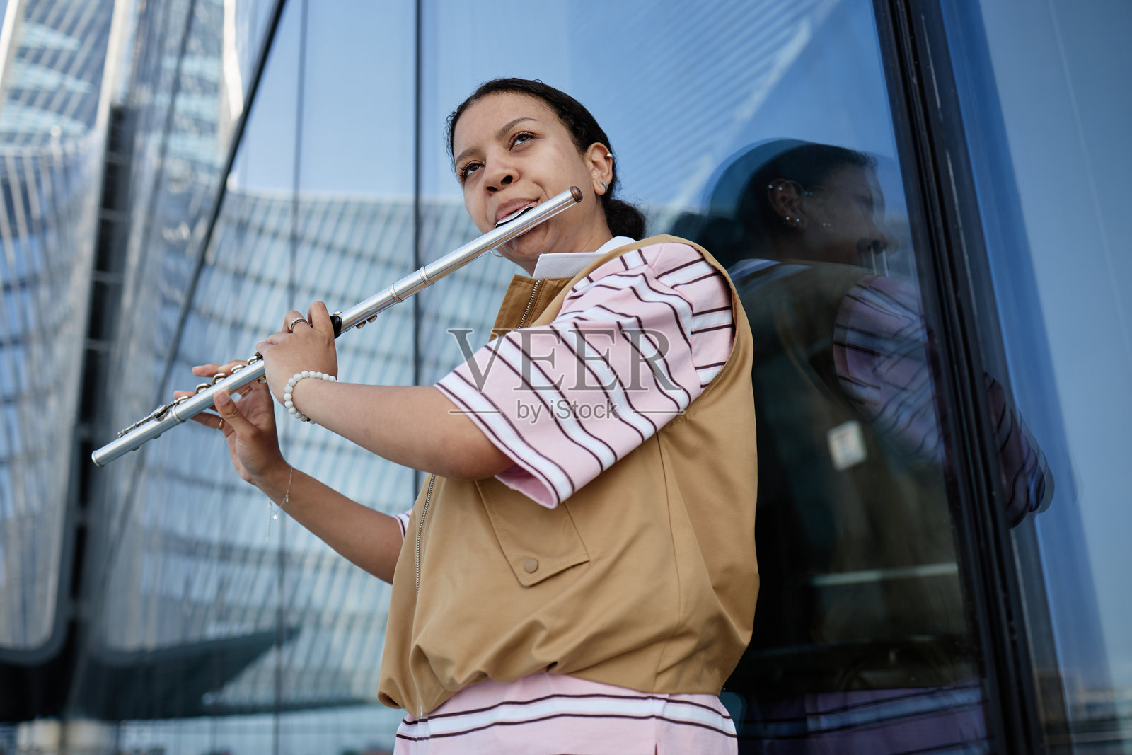 年轻女性在现代玻璃建筑附近户外吹奏长笛照片摄影图片
