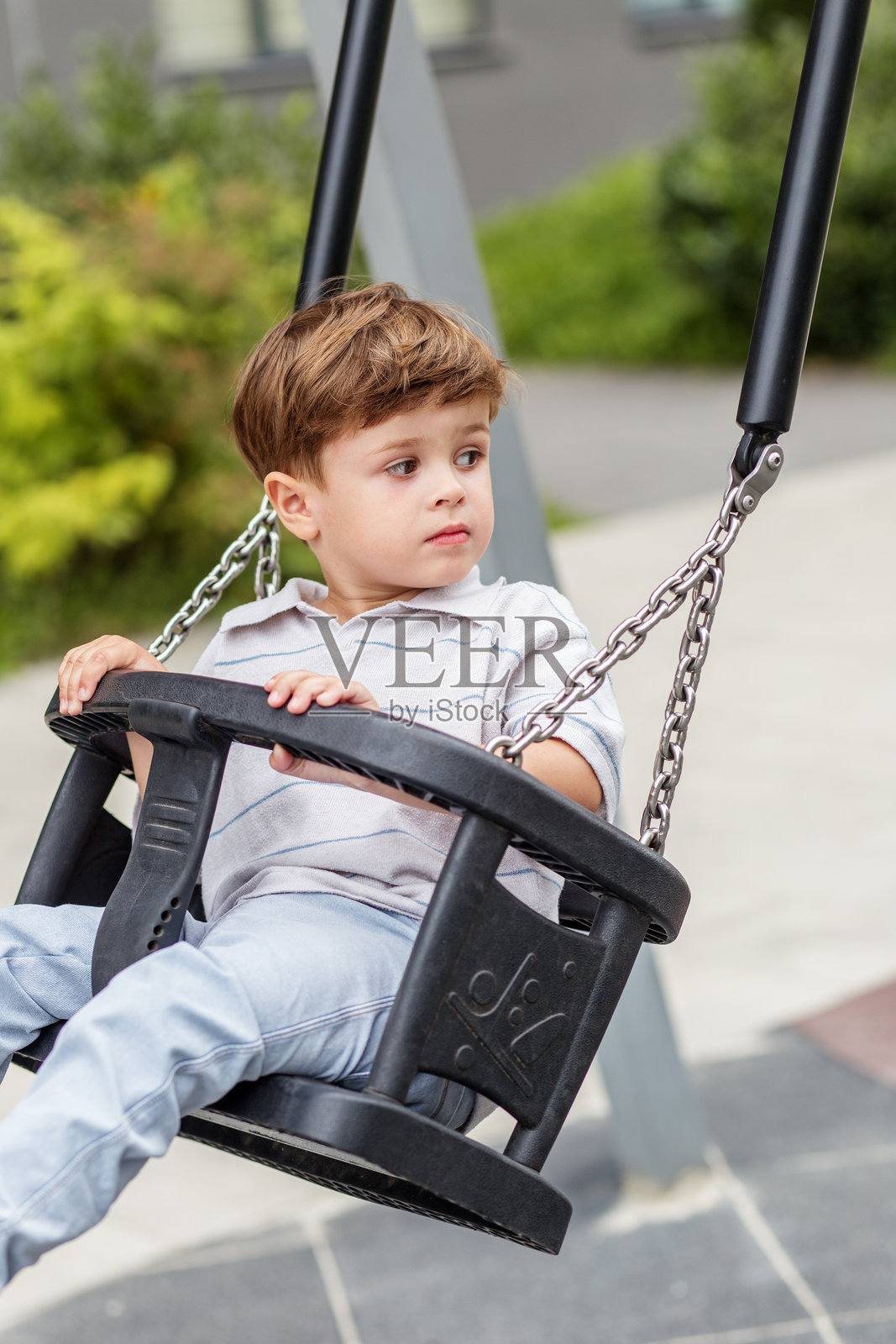 思考的小男孩坐在游乐场秋千上照片摄影图片