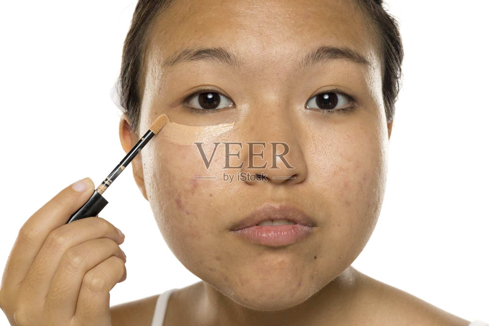 年轻的亚洲女性在眼下涂抹遮瑕膏。照片摄影图片