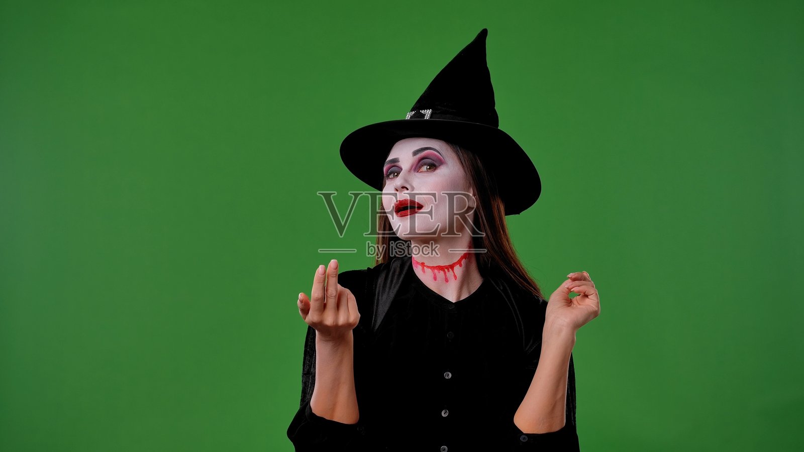 一个化着吸血鬼妆的女巫,穿着黑色斗篷和帽子,做出请过来的手势照片摄影图片