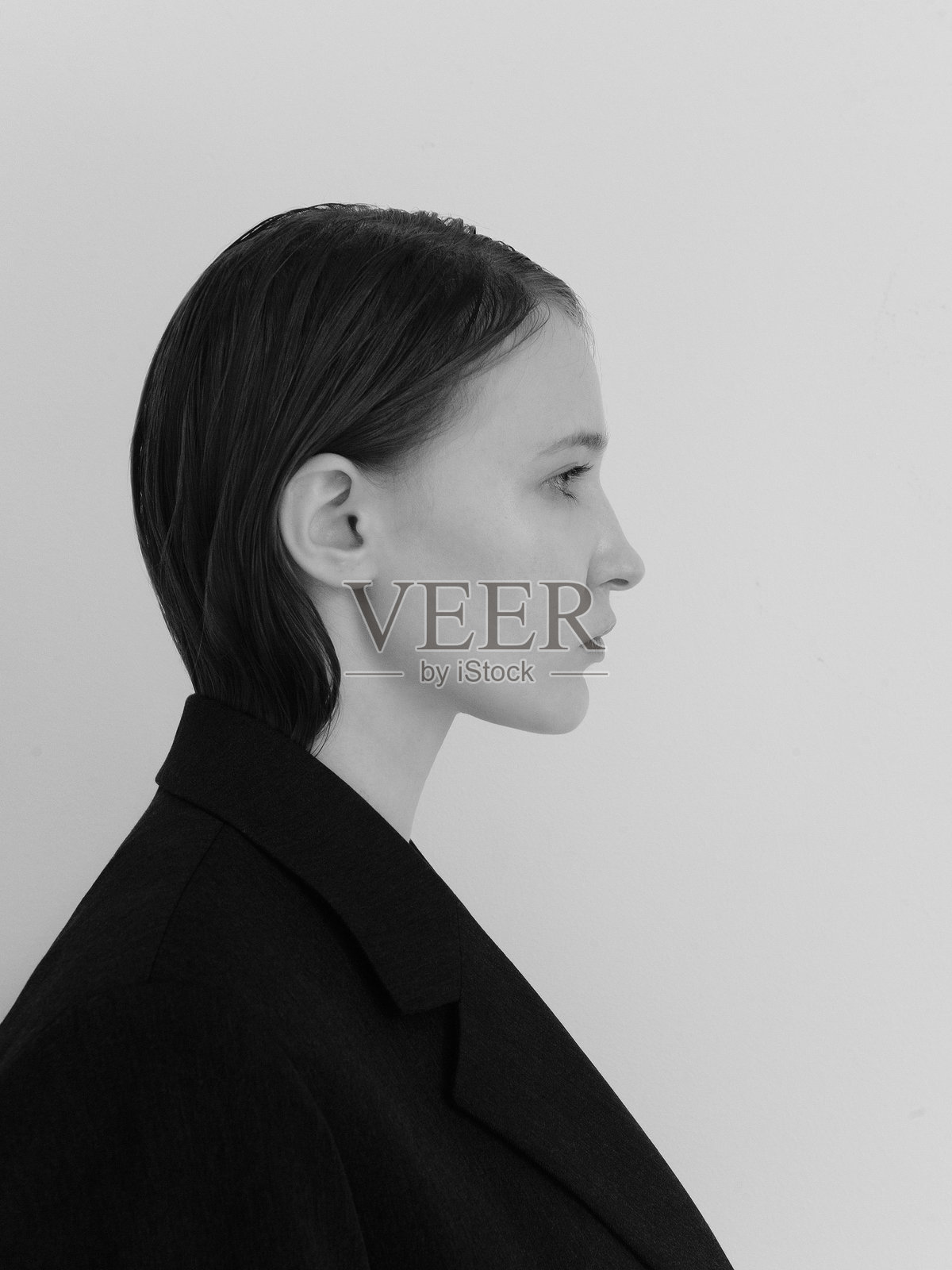 优雅的美丽年轻时尚女性侧面肖像,穿着黑色或深灰色西装,时尚模特在浅白色背景下的工作室肖像。漂亮的年轻女孩化着自然淡妆或完全不化妆,时尚而可爱。照片摄影图片