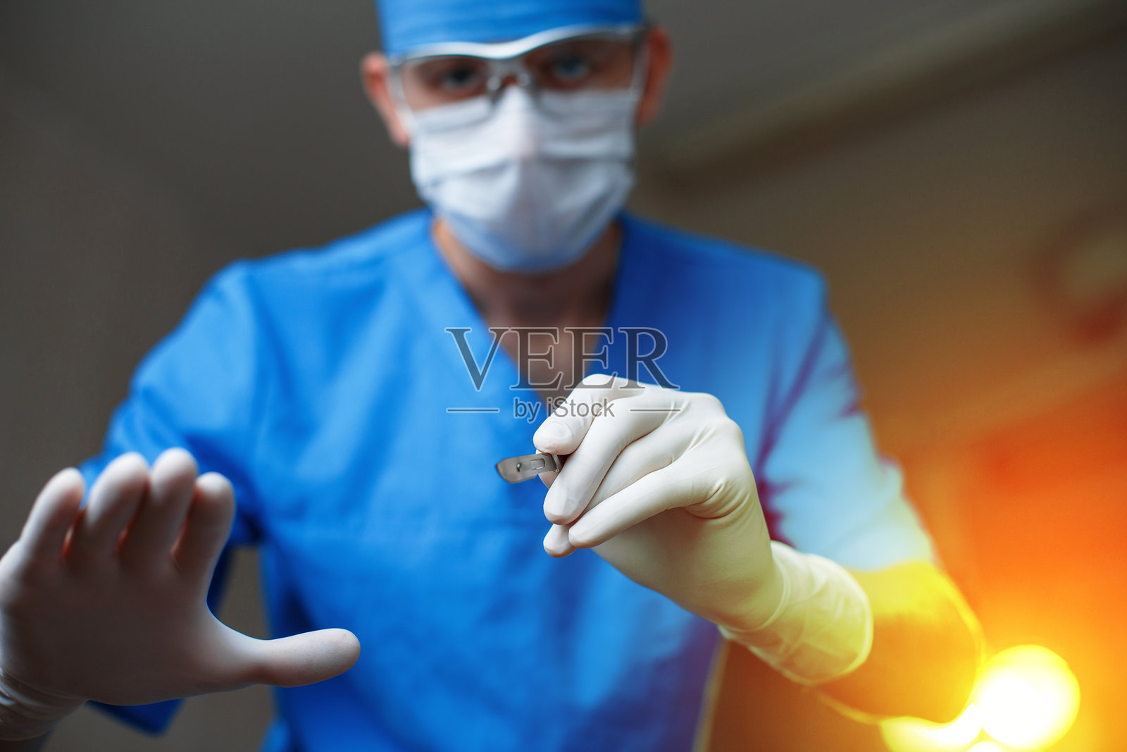 医生手持手术刀,站在明亮的手术灯下。现代外科医生开始手术。照片摄影图片