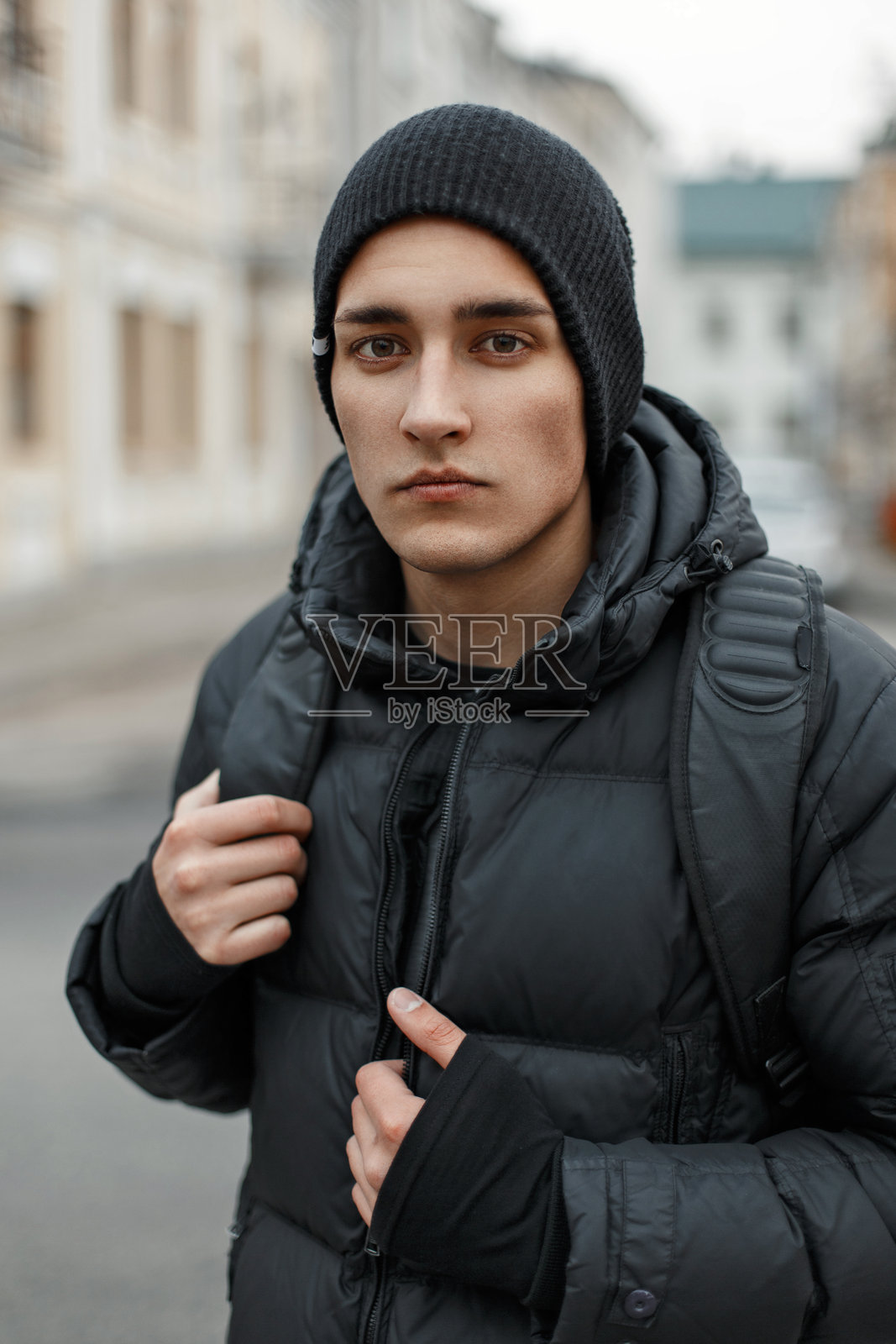 帅气时尚的年轻男子,戴着黑色帽子,穿着冬季外套,背着背包走在街上照片摄影图片