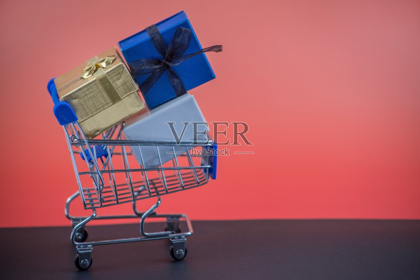 侧面视图的购物车上放着三个礼品盒,背景为黑色和红色。照片摄影图片