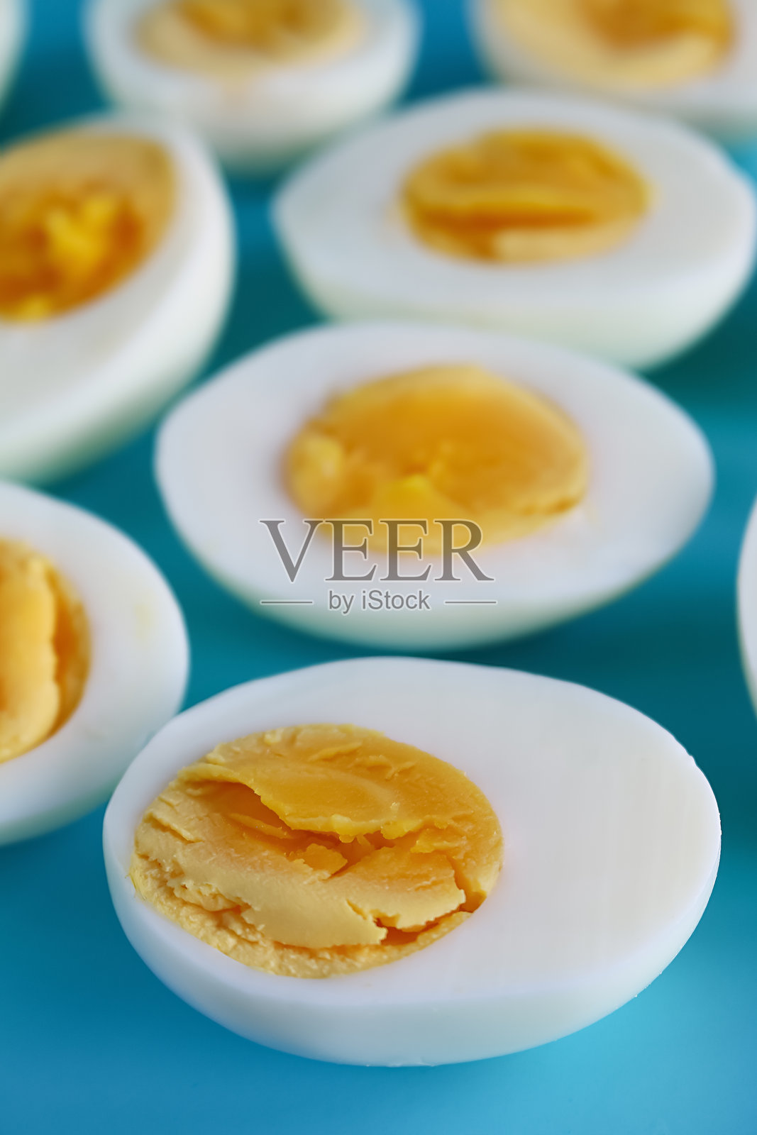 全景图像,展示一组硬煮鸡蛋的蛋白和蛋黄半边,孤立在蓝色背景上,工作室拍摄,健康饮食海报壁纸背景设计,俯视图,重点在前景。照片摄影图片
