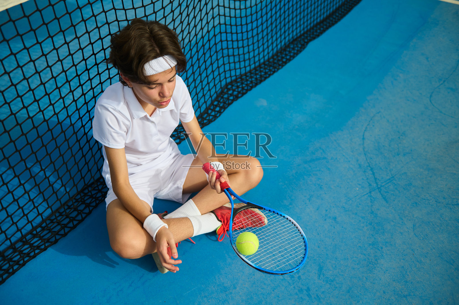 年轻的网球运动员在球场上靠近网休息,沉思中。照片摄影图片