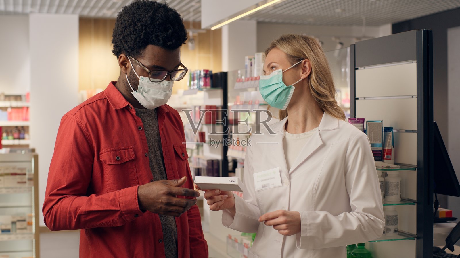 非洲男性顾客在药店,白人女性药剂师戴着口罩,提供抗病毒药物和健康保护,帮助患者应对新冠病毒感染。照片摄影图片