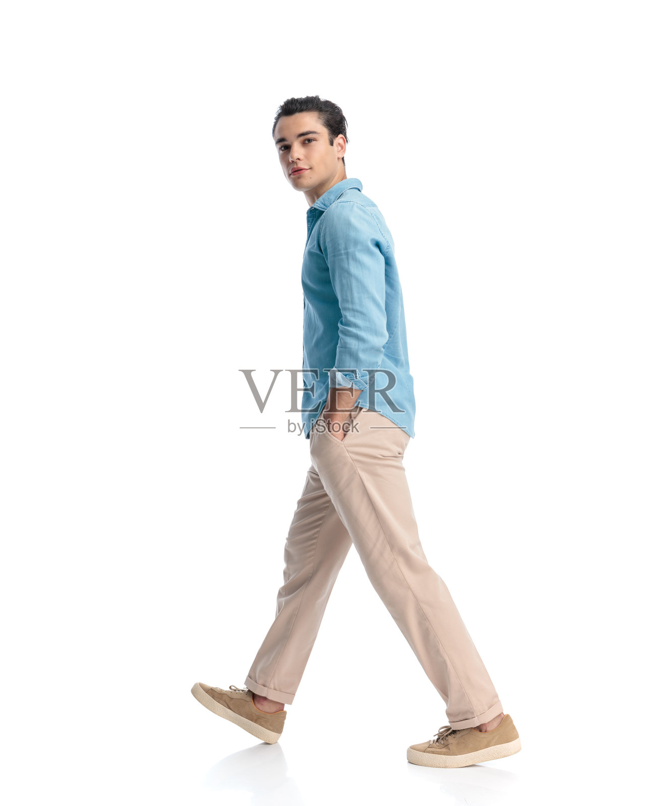 侧面视角的快乐年轻男子,穿着蓝色牛仔衬衫,手插在口袋里走路照片摄影图片