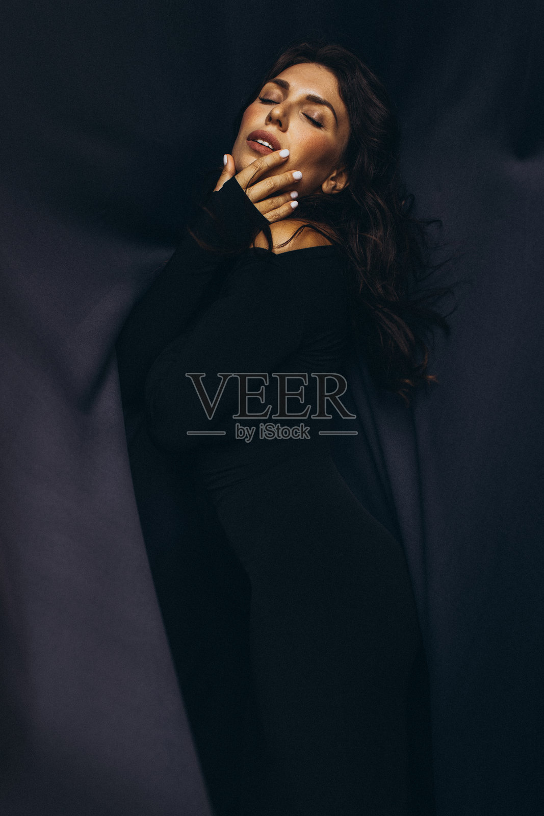 身穿黑色服装的女性在柔和的灯光下优雅地摆姿势,面带宁静的表情照片摄影图片