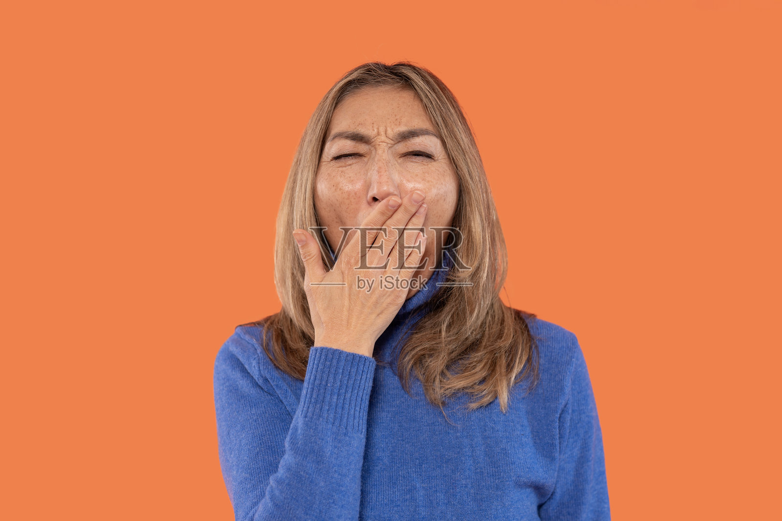 在明亮的橙色背景前,打哈欠的女性在家中午休时表达疲惫。照片摄影图片
