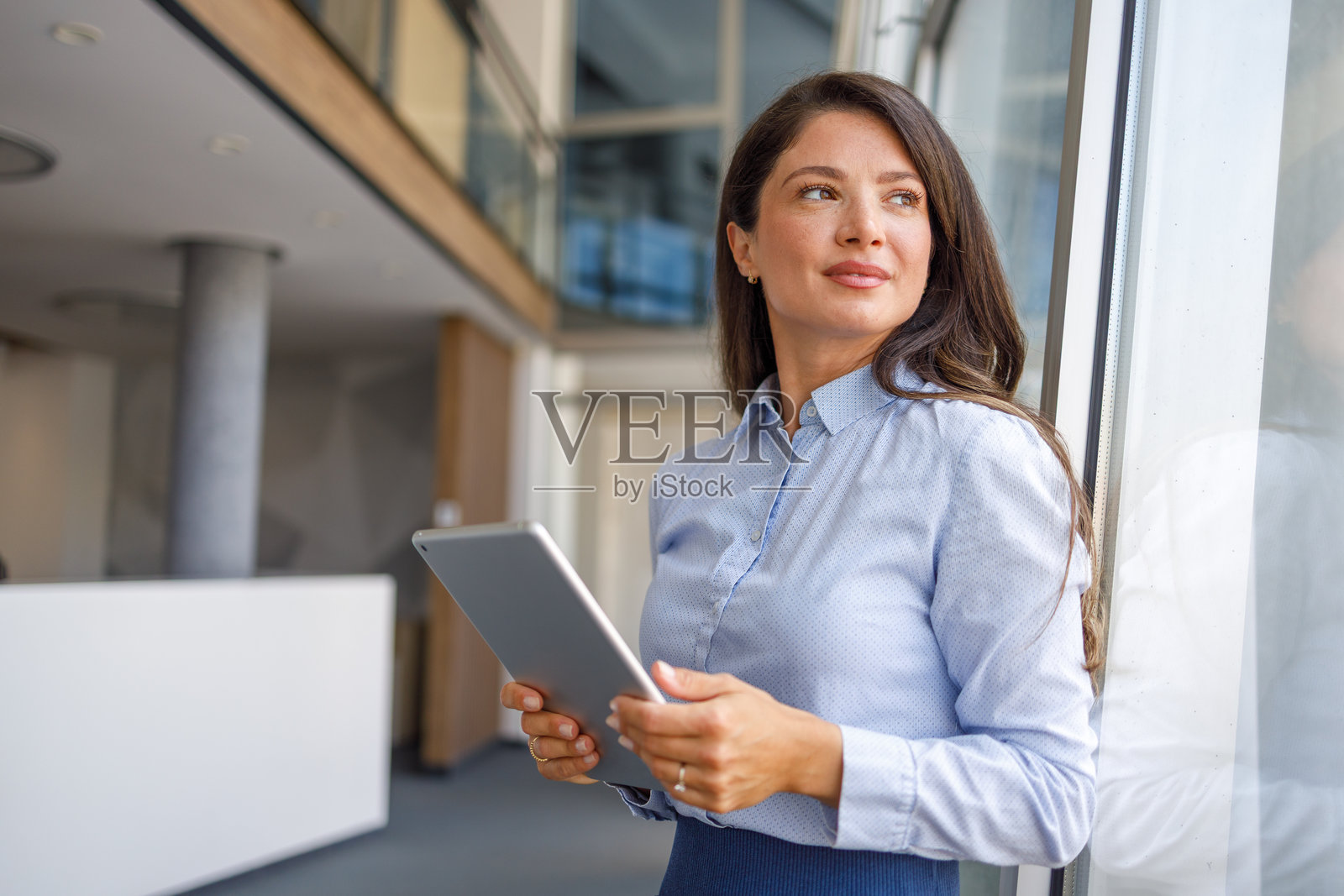 女商人手持数字平板,望向办公室窗外照片摄影图片