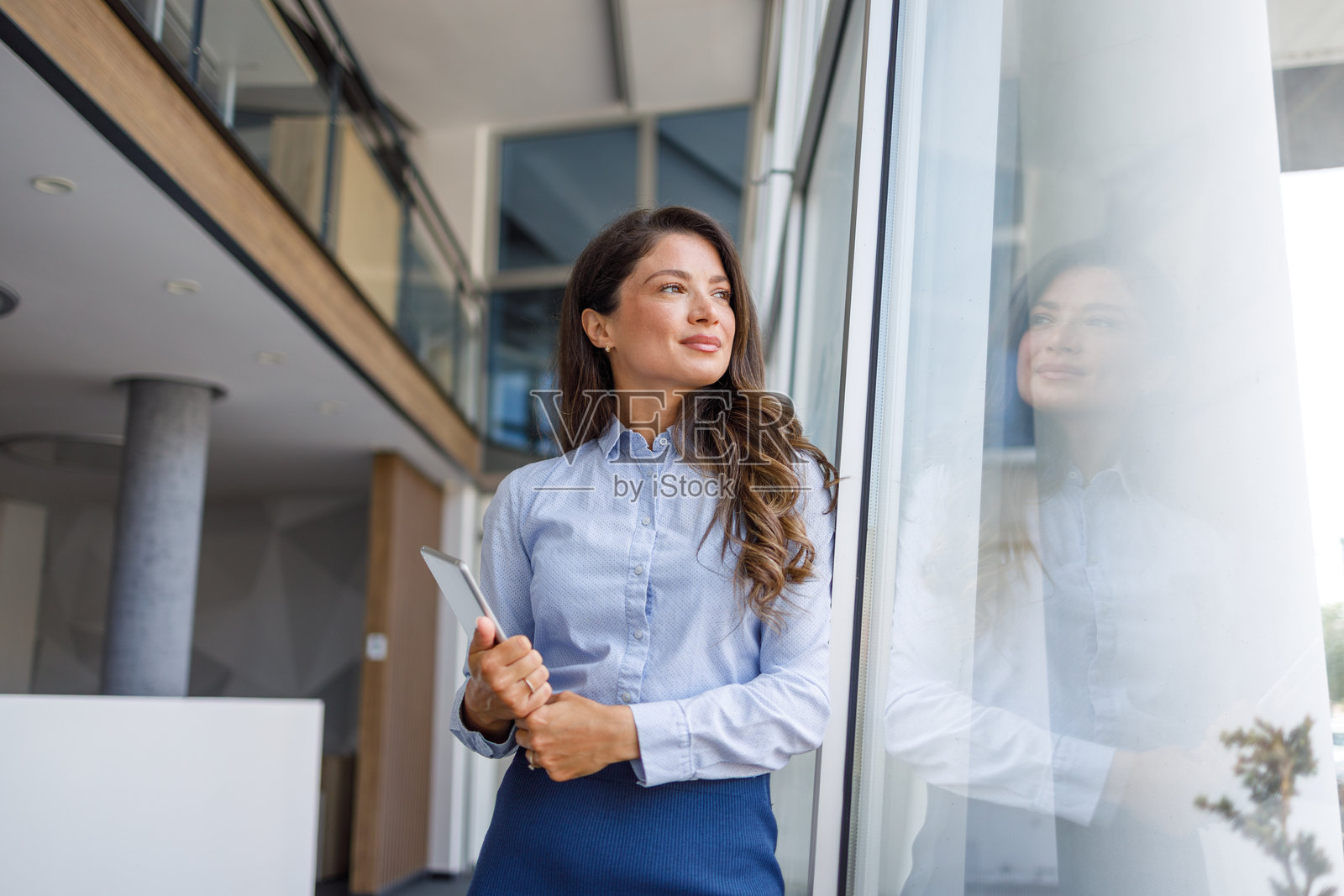 女商人手持数字平板,望向办公室窗外照片摄影图片