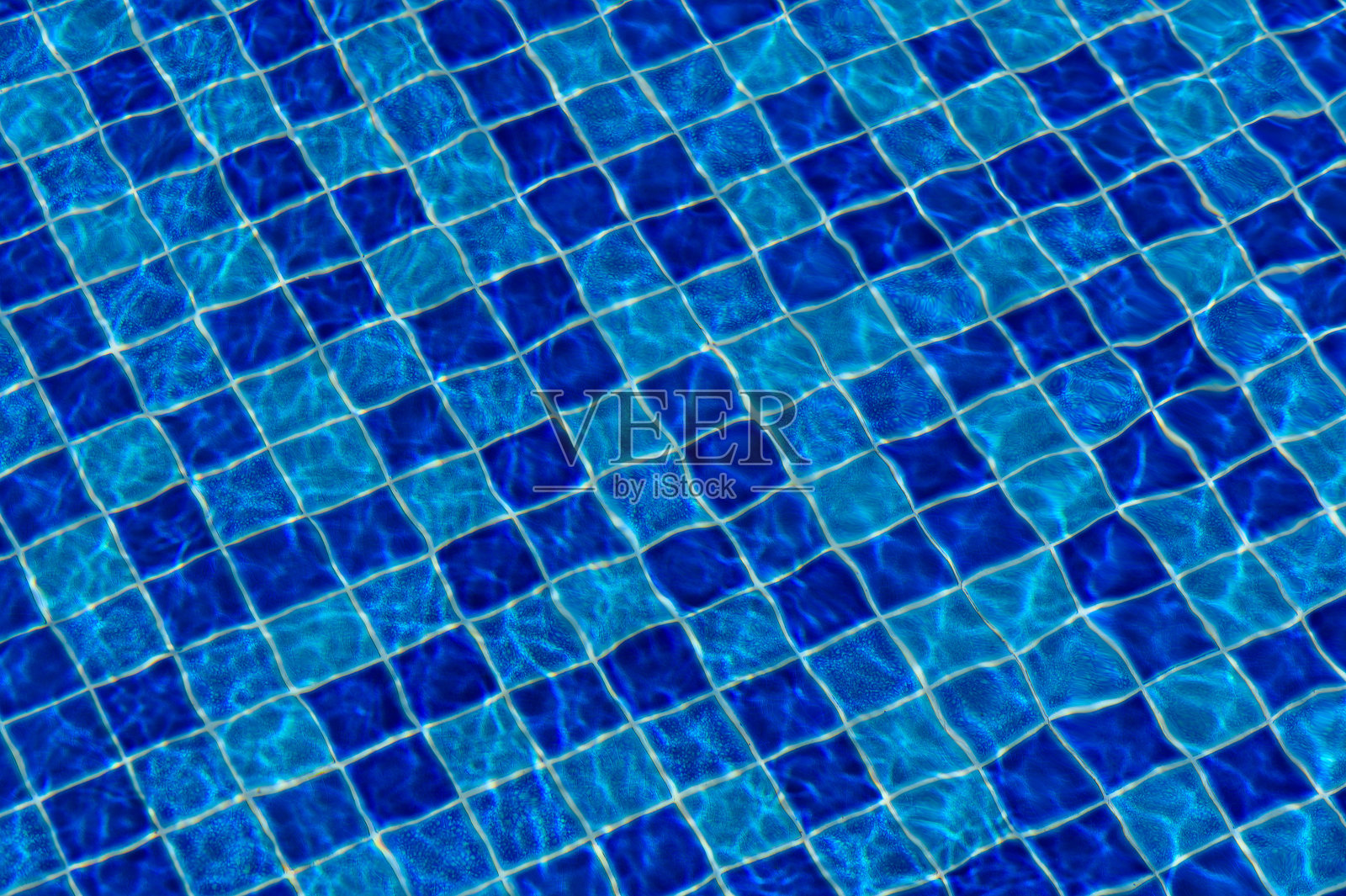 夏日午后,阳光照耀下,波光粼粼的蓝色水面映照在铺有瓷砖的泳池上。照片摄影图片