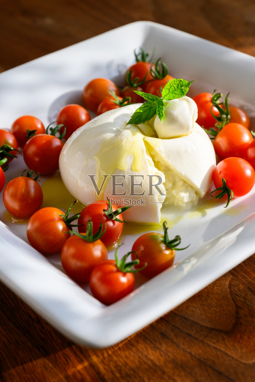 在下午晚些时候的阳光下,Burrata和田间成熟的樱桃西红柿放在拼盘上照片摄影图片