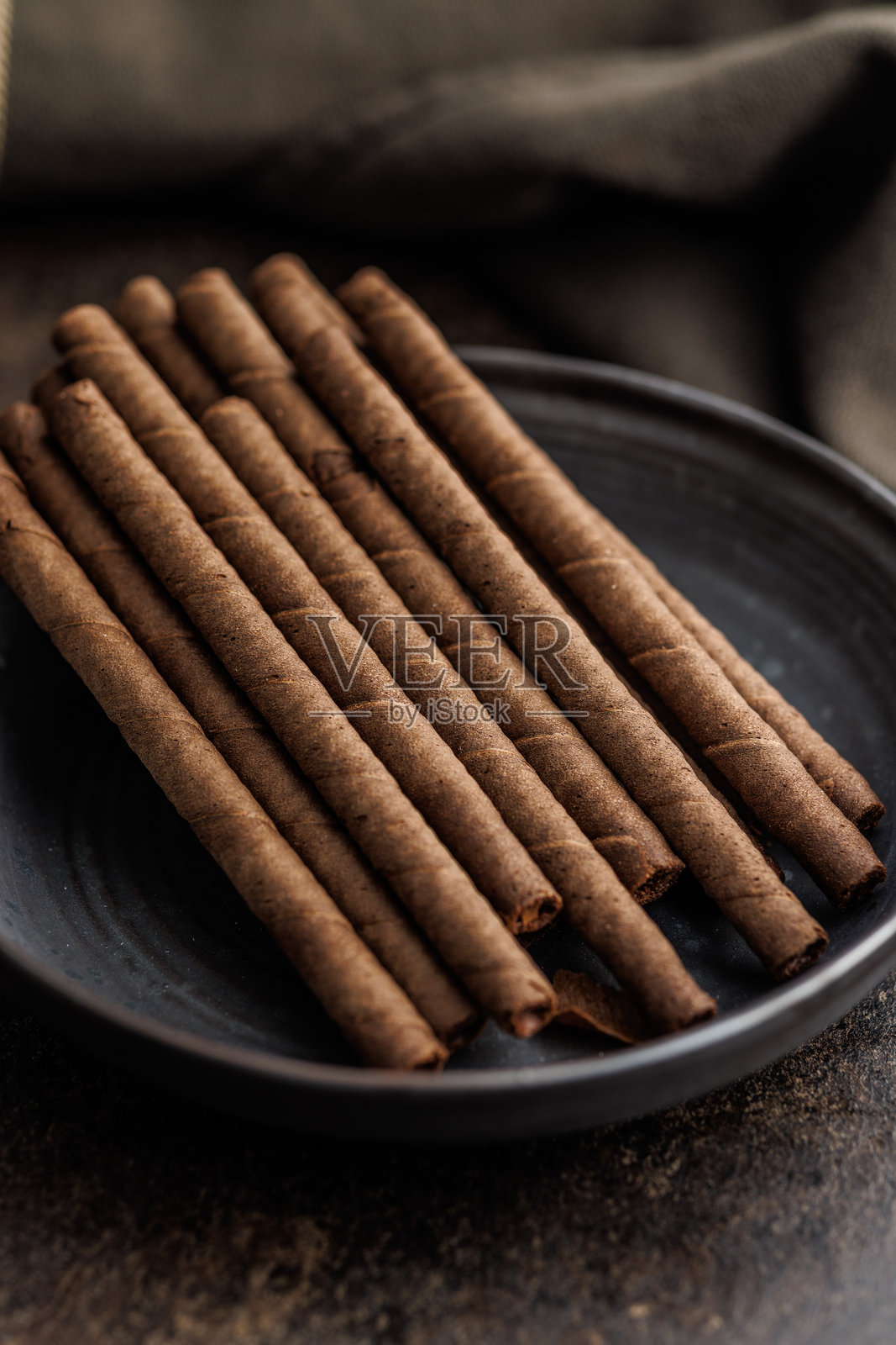 黑桌子上盘子里的巧克力威化卷。照片摄影图片