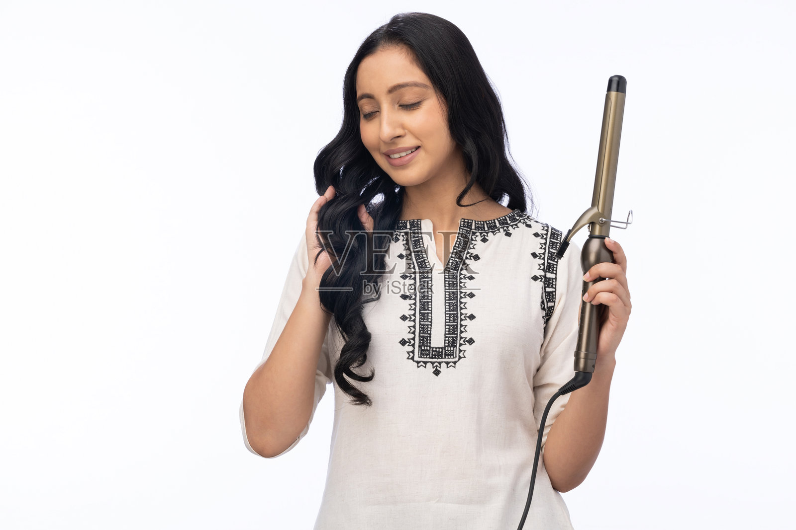 年轻女性使用热卷发棒的肖像,背景为白色。照片摄影图片