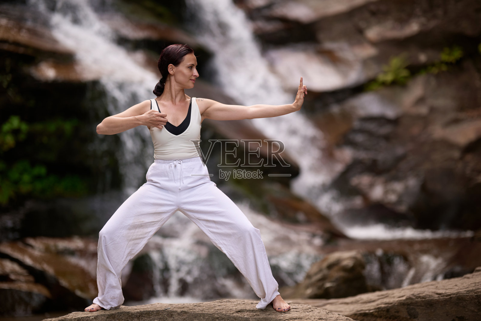 在日落时分,女人在瀑布和河流旁缓慢地练习太极,展现了自然中的和谐、平衡与健身。照片摄影图片