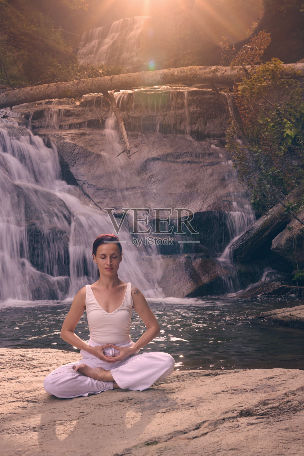 年轻女性坐在热带瀑布下的莲花坐姿中,冥想时展现出平静的力量和正念,完全与自然的能量、宁静和内心的平衡相连接。照片摄影图片