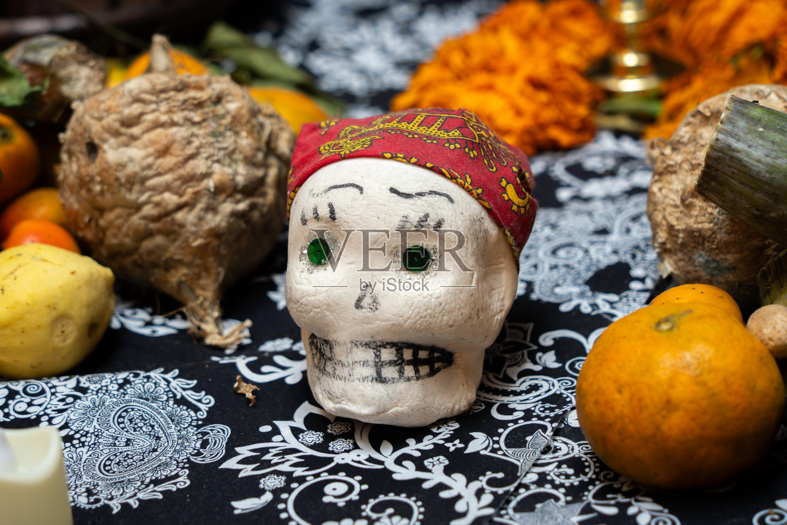 一个戴着头巾的骷髅坐在桌子上,周围摆放着各种水果。这是墨西哥的亡灵节庆祝活动,纸花工艺,供品,拉卡特里娜。照片摄影图片