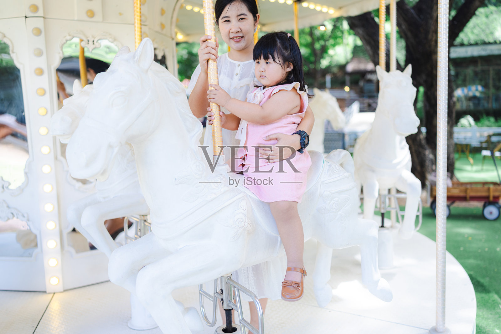 一位可爱的亚洲母亲和女儿在游乐园快乐地骑旋转木马,幸福的家庭,迷人的女性和可爱的小女孩在假期旅行时感到快乐和放松。照片摄影图片