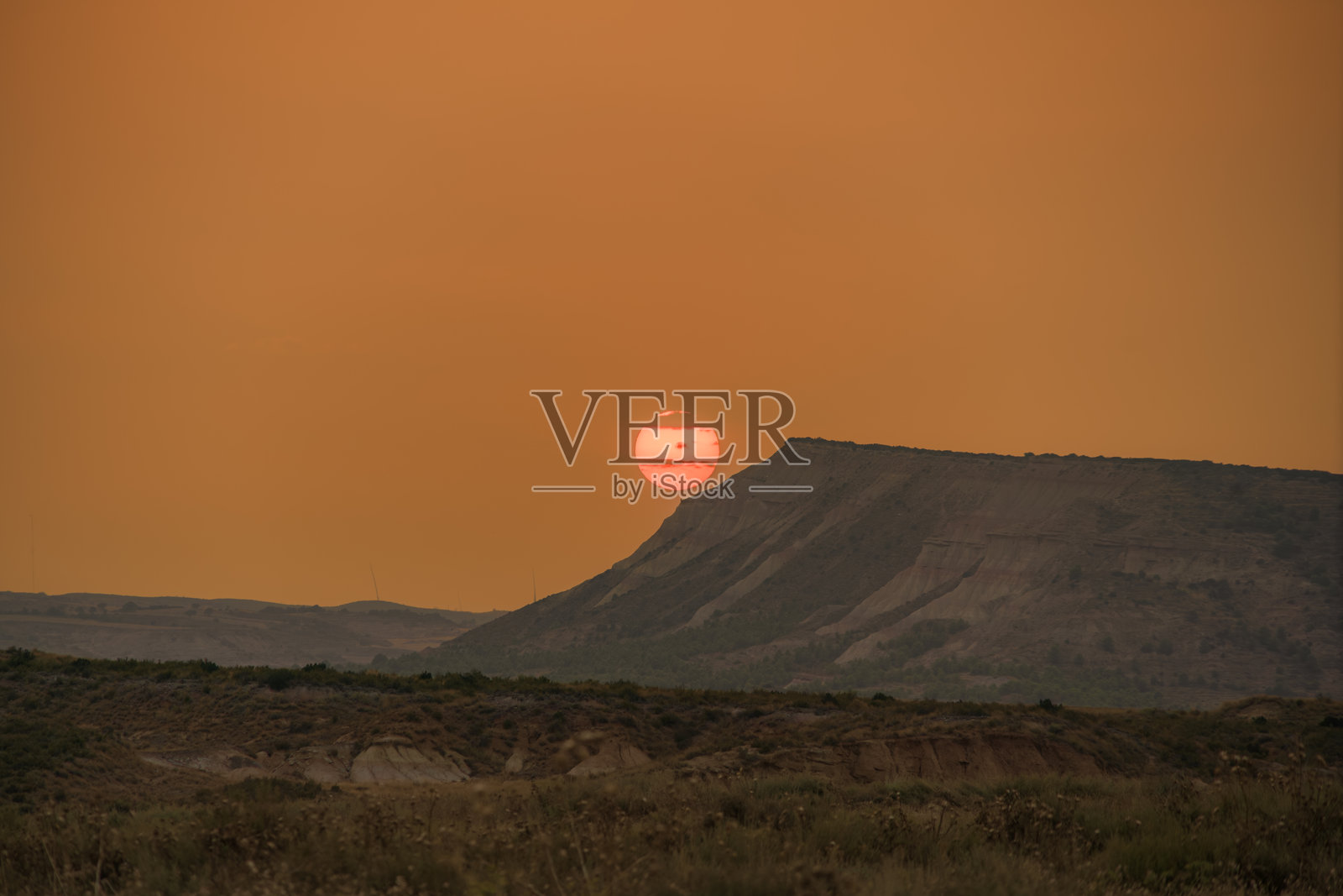 沙漠日落,红色太阳在山脊后面,创造出橙色的天空。干旱的景观,戏剧性的晚间光线,偏远的荒野,富有气氛的沙漠。照片摄影图片