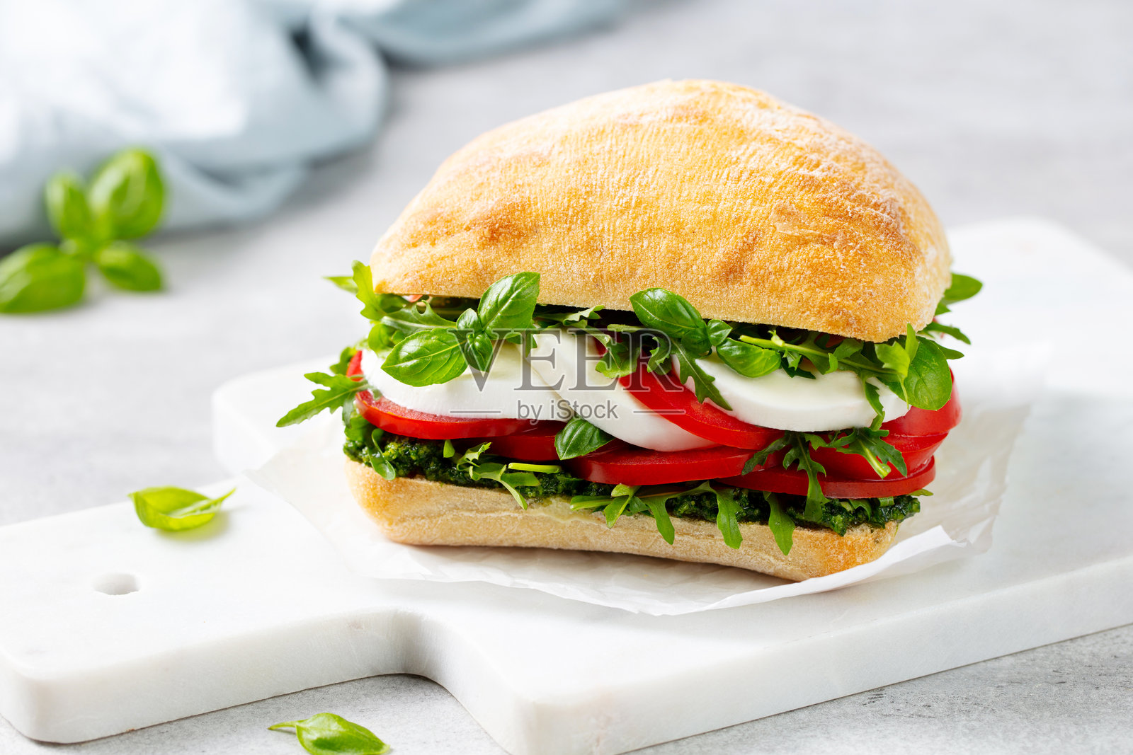 马尔堡餐盘上的恰巴塔三明治,配有莫扎里拉奶酪、西红柿、香蒜酱和新鲜罗勒。浅灰色背景。特写。照片摄影图片