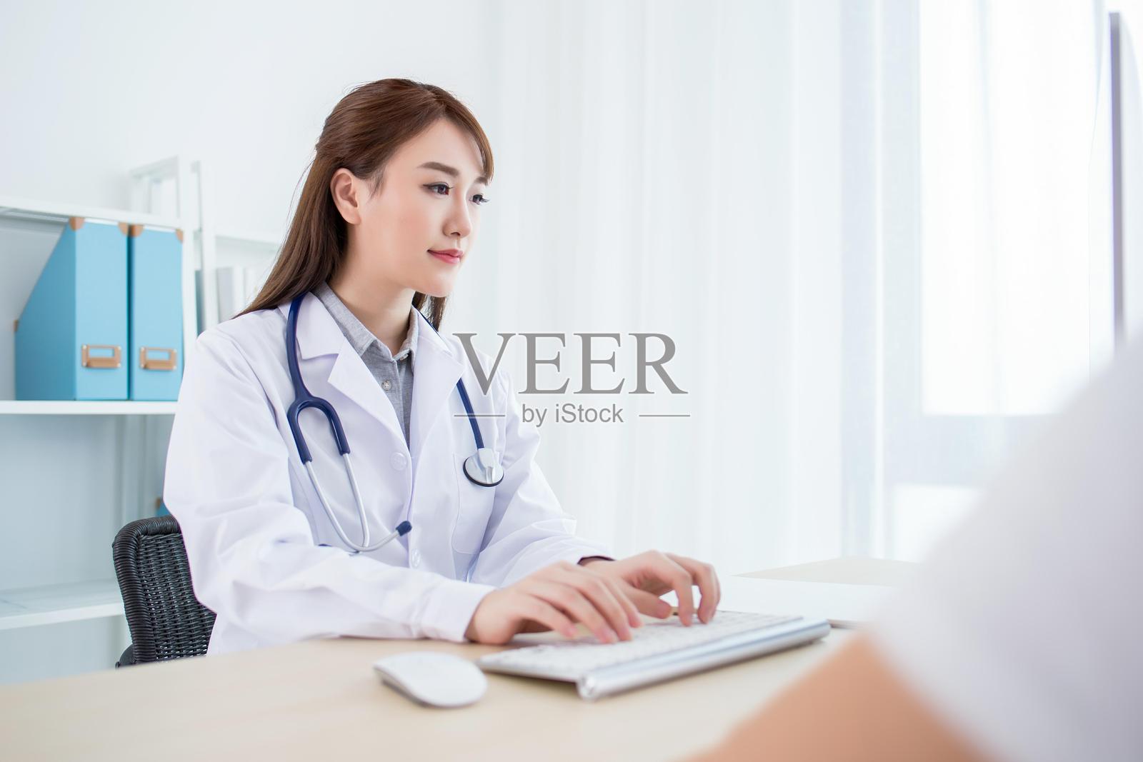 穿着白大褂的女医生在桌子上使用电脑工作照片摄影图片
