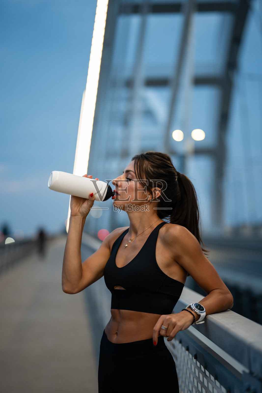 黄昏时分,运动女性在桥上训练后喝水照片摄影图片