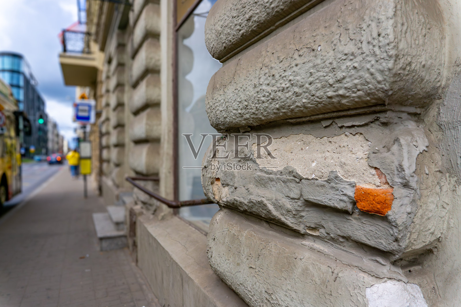 受损的公寓外立面,砖墙和橙色涂料细节,位于繁忙的街道旁,公交车经过。照片摄影图片