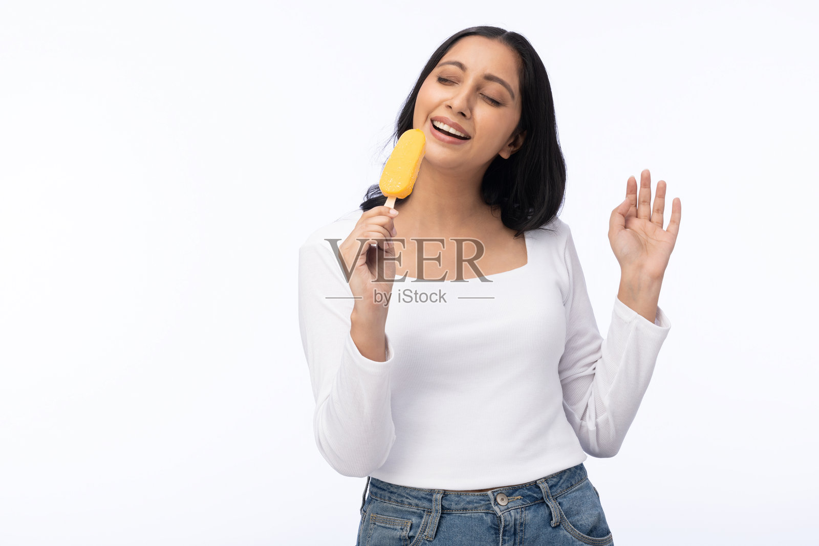 年轻女性穿着现代服装,享用芒果冰淇淋的肖像,背景为白色。照片摄影图片